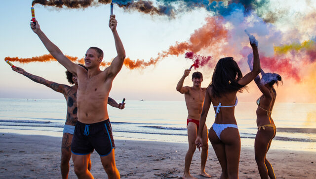 Group of friends having fun running on the beach with smoke bombs